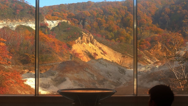 A person sitting by a window overlooking a mountainous landscape with autumn foliage. - Dai-ichi Takimotokan (Noboribetsu)