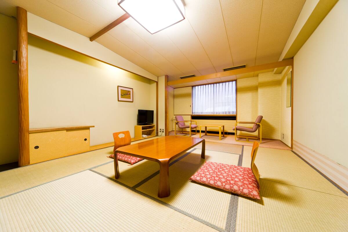 A traditional Japanese tatami room with a low table, two chairs, a television, and a sliding door.