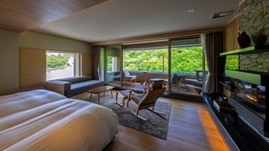 A modern hotel room with a large bed, a seating area with a table and chairs, a fireplace, and a balcony with a view of greenery. - Dai-ichi Takimotokan (Noboribetsu)