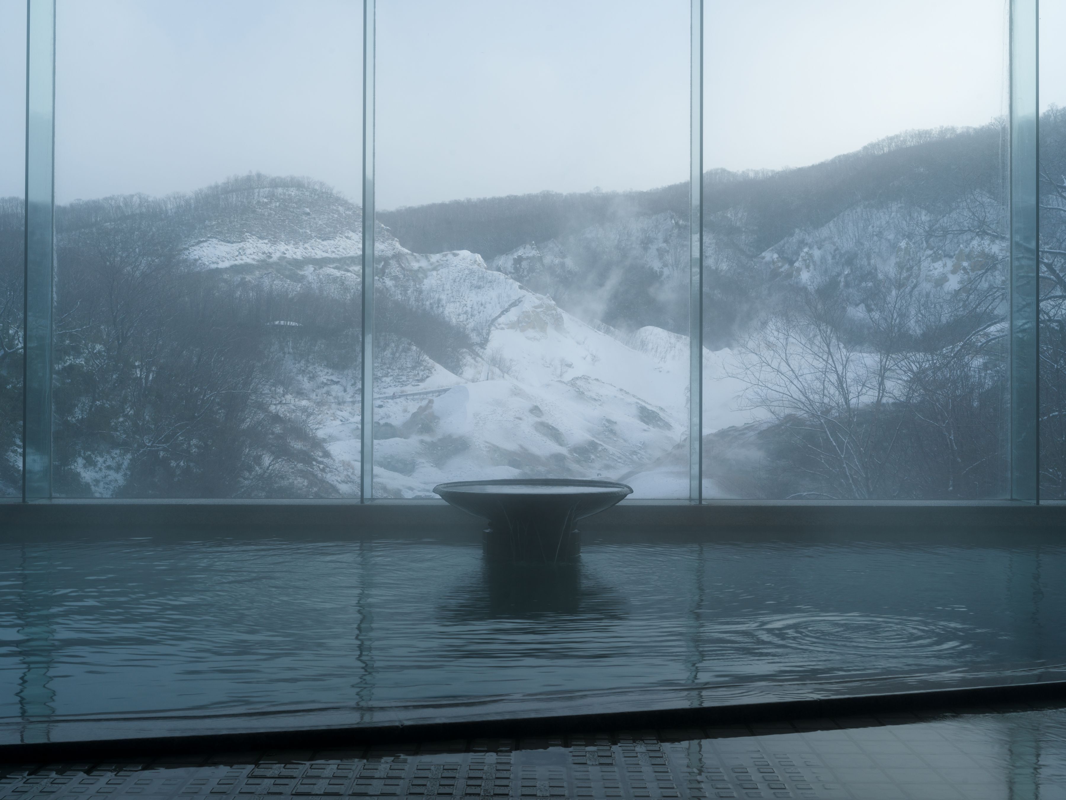 A view through a large window of a snowy landscape with a water feature in the foreground.