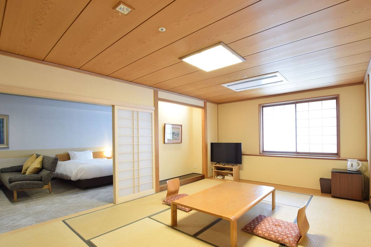 A traditional Japanese room with tatami flooring, a low wooden table, a sofa, a bed, a TV, and a sliding door.