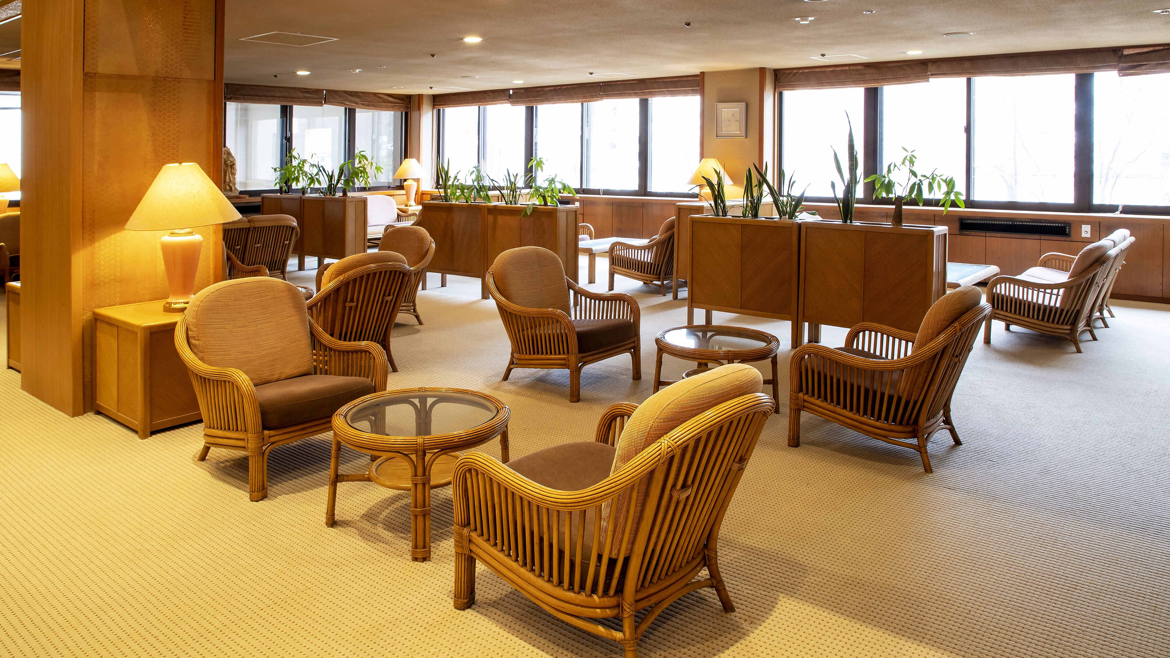 A hotel lobby with wicker furniture, large windows, and potted plants.