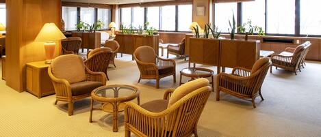 A hotel lobby with wicker furniture, large windows, and potted plants.