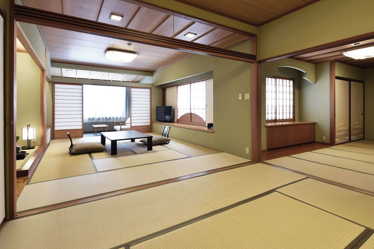 A traditional Japanese room with tatami flooring, a low table with cushions, a television, and sliding doors.