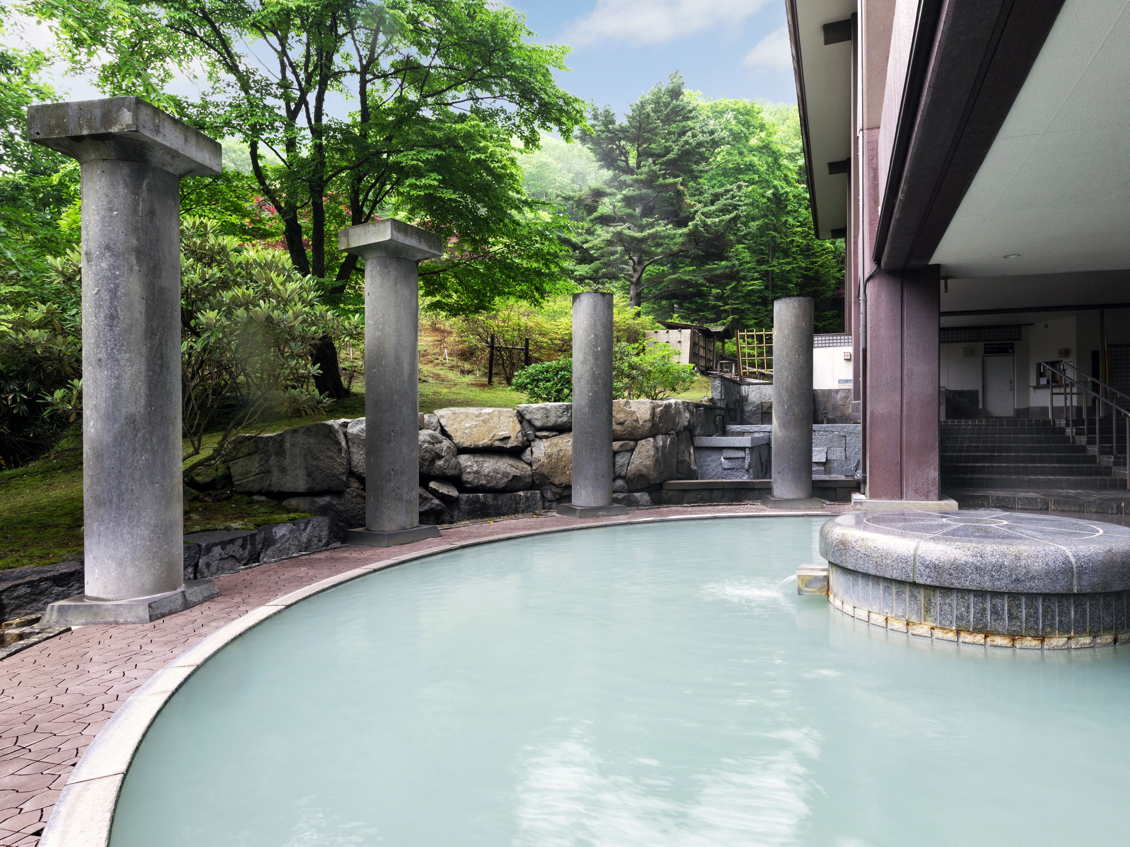 A pool with stone pillars, a stone wall, and a building entrance with stairs.