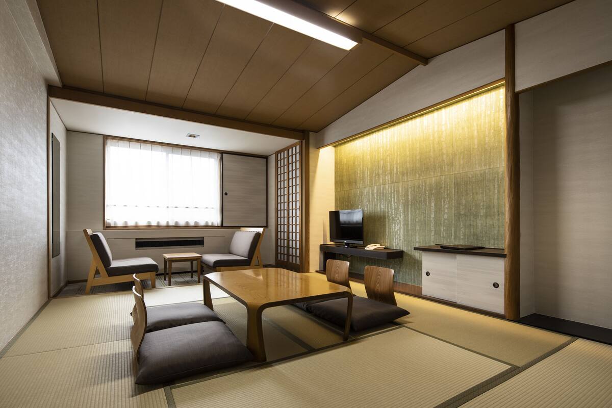 A traditional Japanese-style room with tatami flooring, a low table with cushions, a television, and sliding doors.