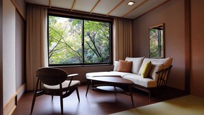 A room with a sofa, a chair, a small table, and a large window with a view of trees. - Dai-ichi Takimotokan (Noboribetsu)