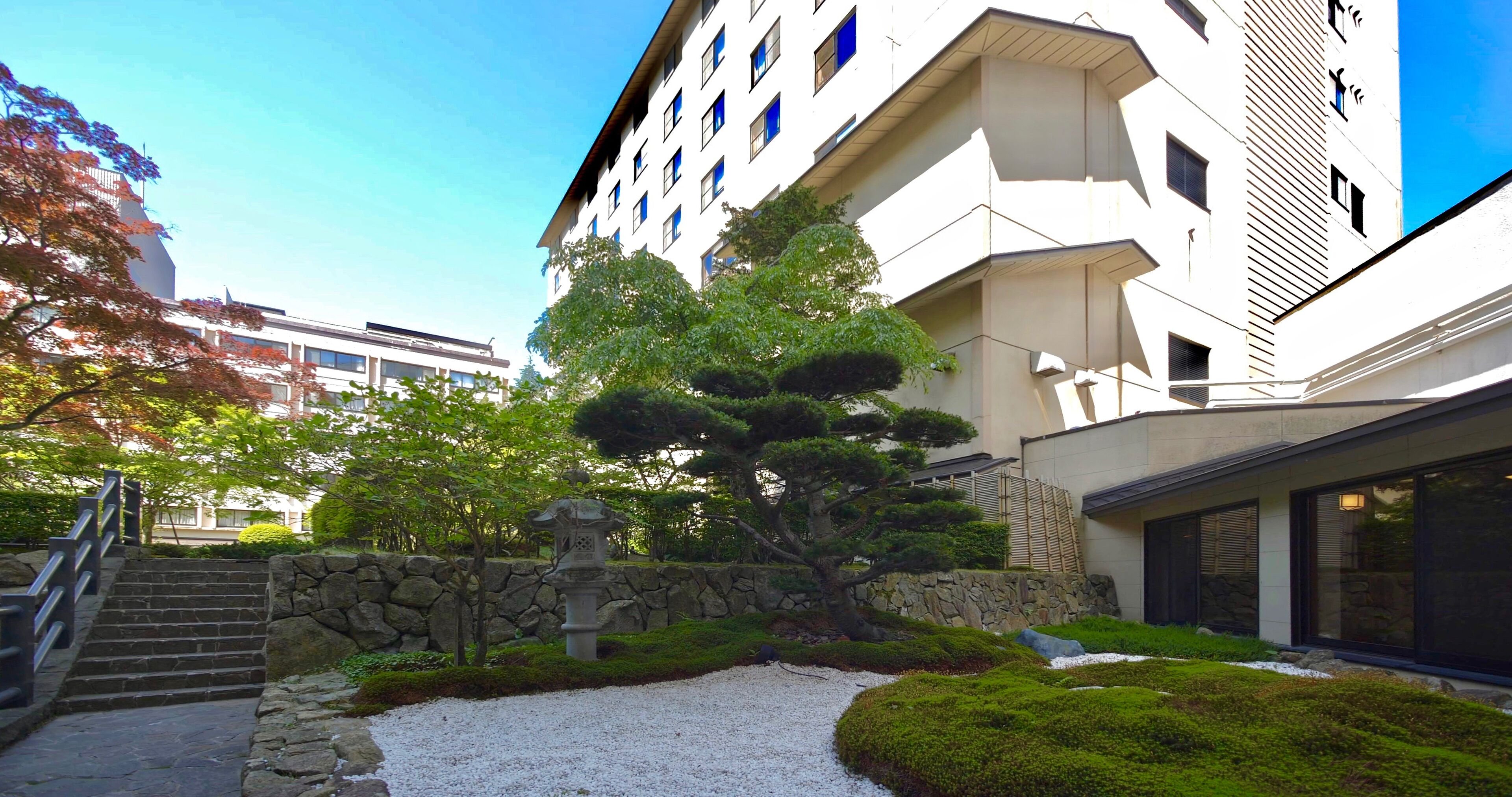 A modern building with a stone wall and a well-maintained garden with a stone lantern and a bonsai tree.