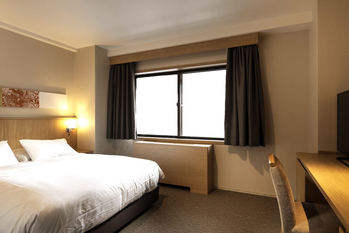 A hotel room with a large bed, a desk, and a window with curtains.