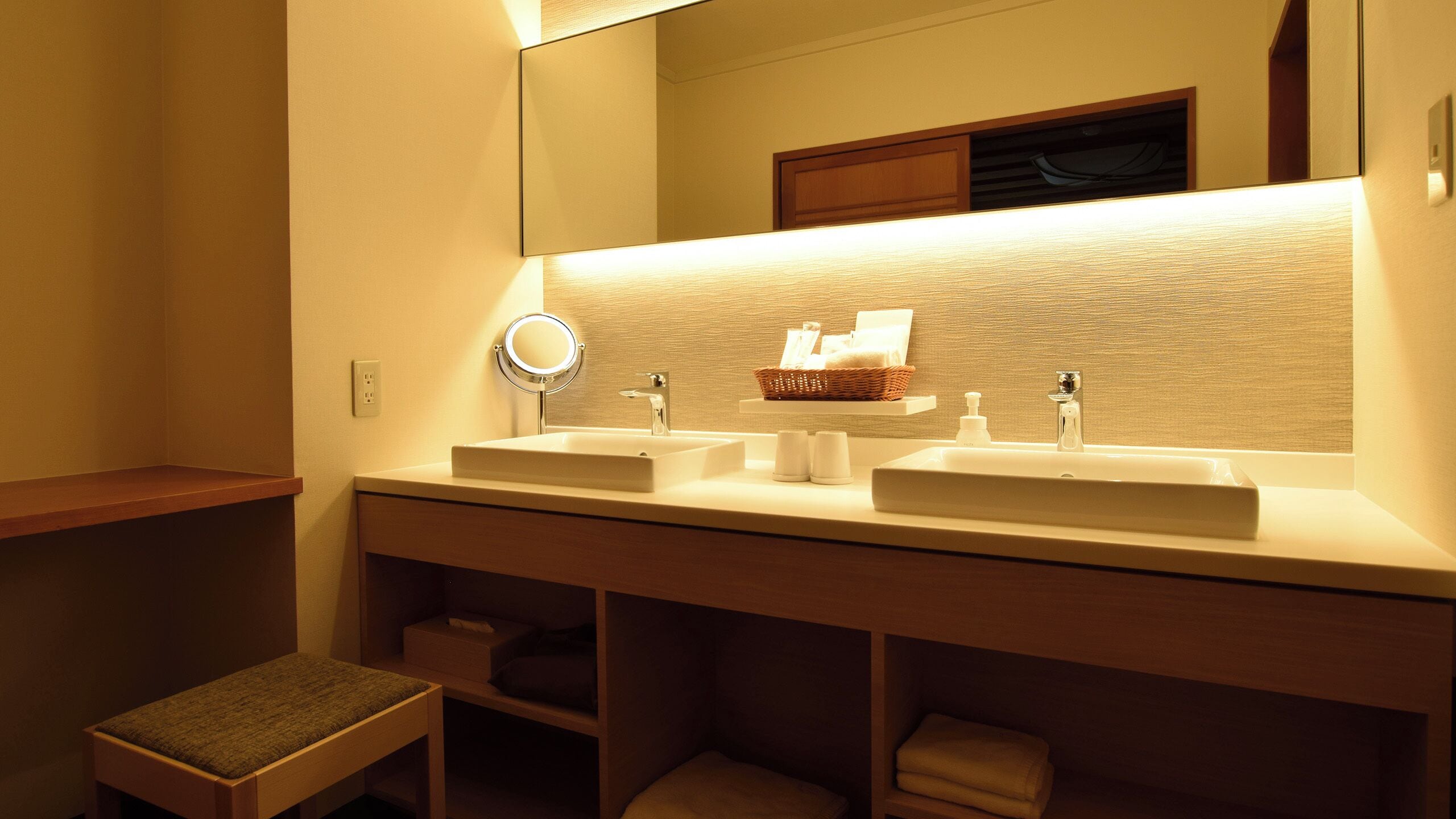 A bathroom with two sinks, a mirror, and a shelf with toiletries.
