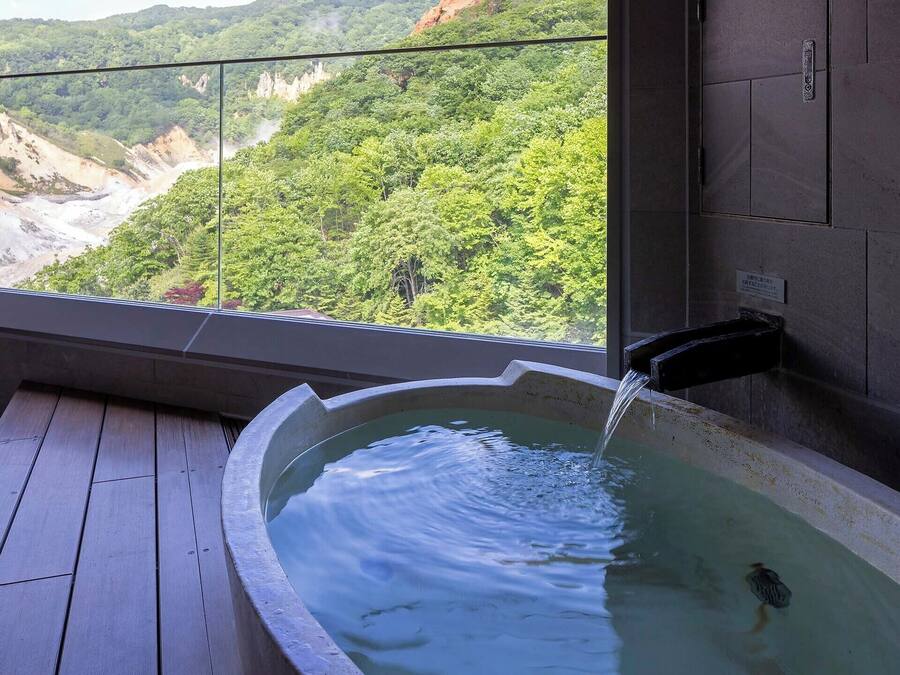 A hot tub with a waterfall feature, a wooden deck, and a view of a forested valley.