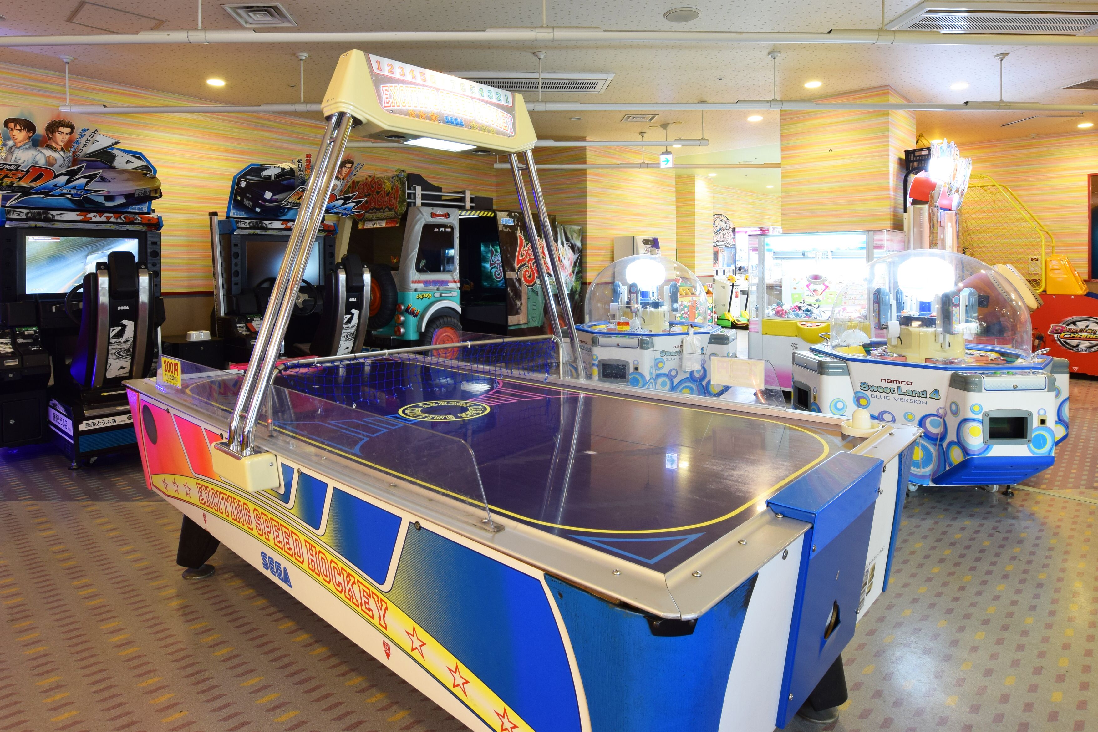 Un salón recreativo con diversas máquinas de juego, incluyendo un juego de lanchas rápidas y un juego de carreras.