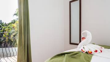A hotel room with a balcony, a bed with a green bedspread, and a white towel with rose petals on it.