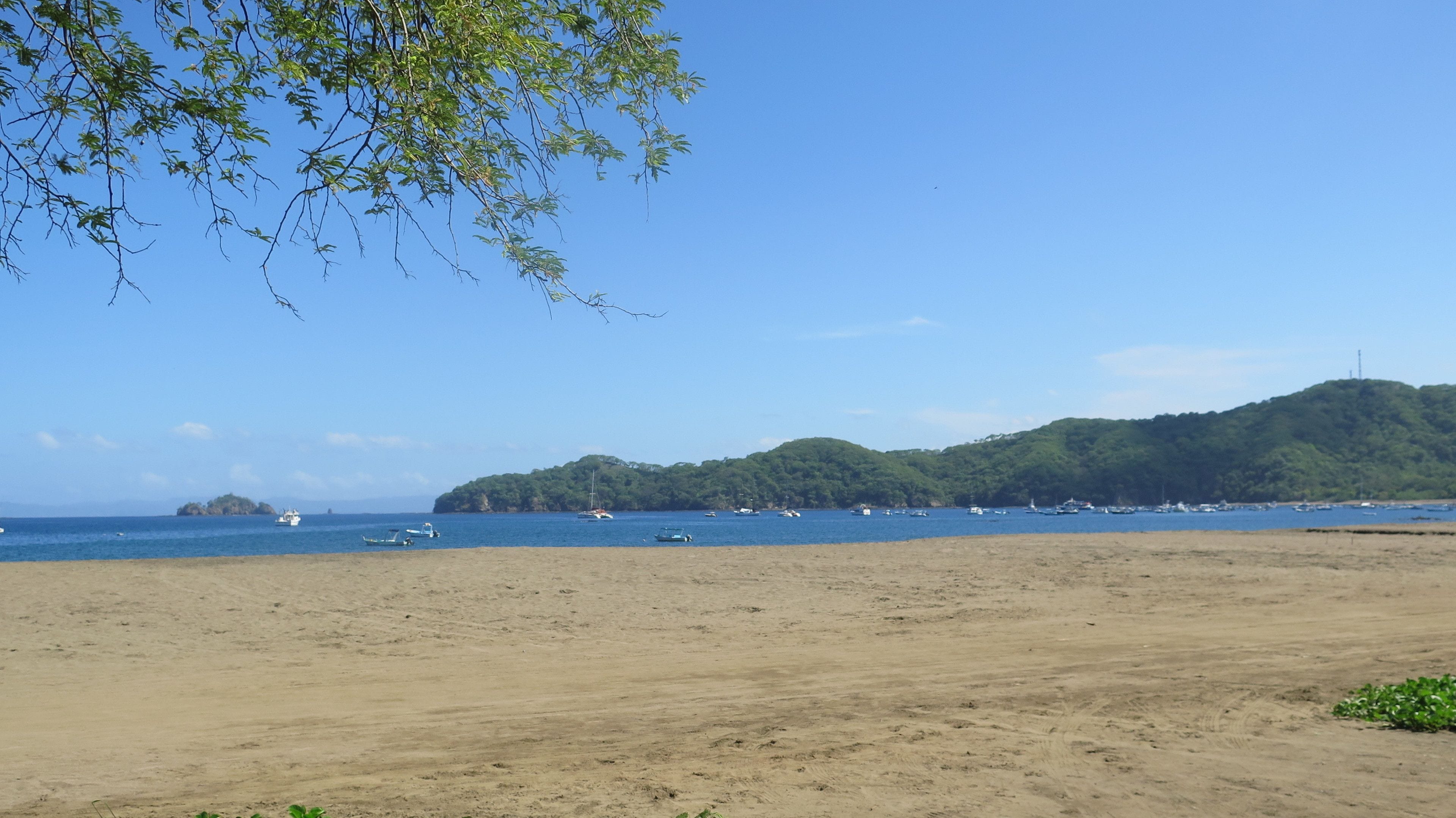 Una playa con barcos en el agua y una colina al fondo.