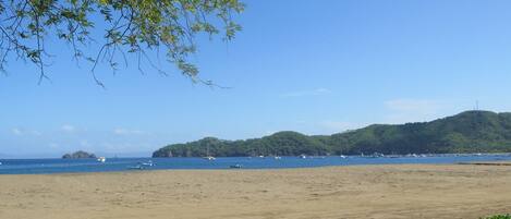 Una playa con barcos en el agua y una colina al fondo.