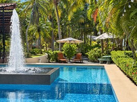A swimming pool with a water fountain, surrounded by palm trees and outdoor seating.