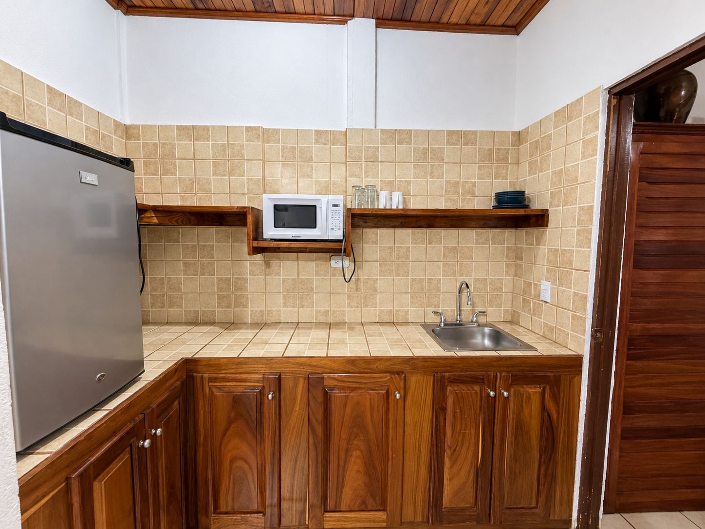Een keuken met een ingebouwde magnetron, een roestvrijstalen spoelbak, houten kastjes en een houten plafond.