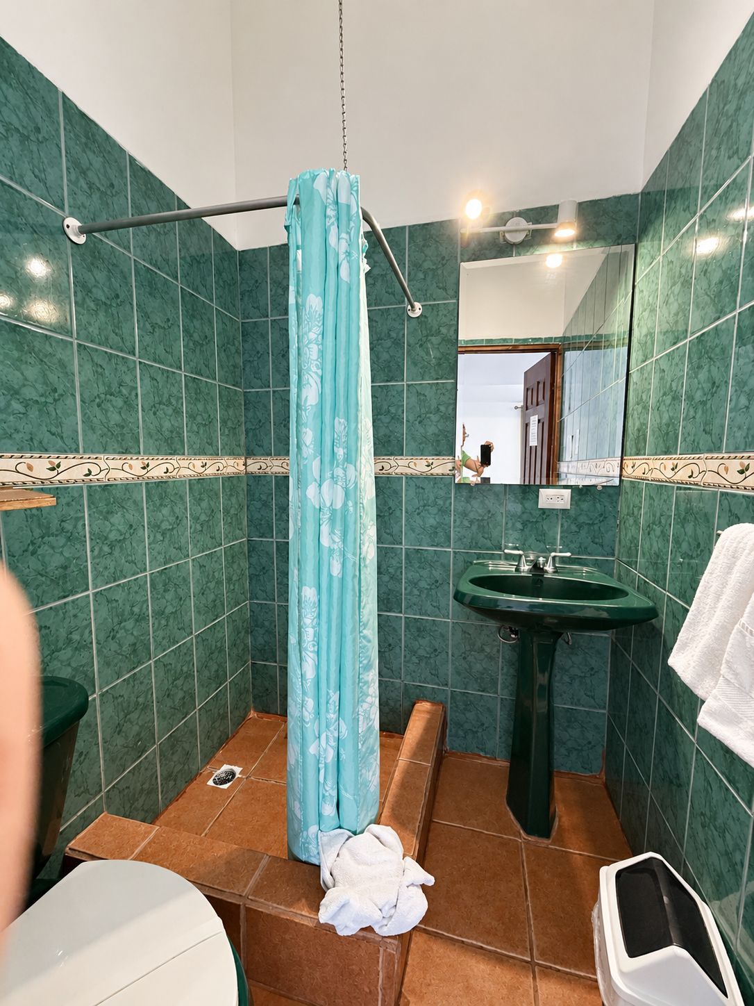 A bathroom with green marble walls, a shower curtain, a sink, and a toilet.