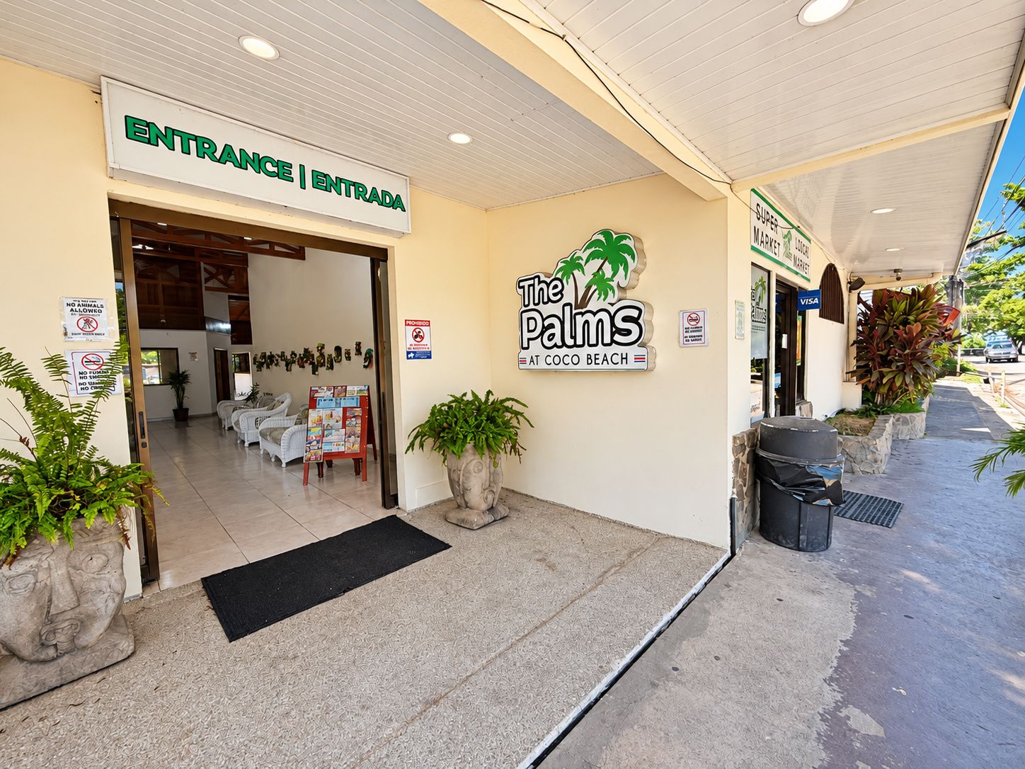 Entrada de un hotel con un letrero que dice 'ENTRANCE | ENTRADA', un logotipo de palmera y un letrero de 'VISA'.