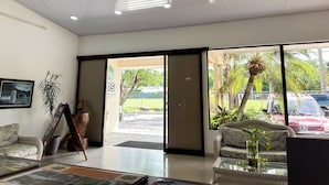 A spacious lobby with a large glass door leading outside, a wicker sofa, a framed picture on the wall, and a potted plant.