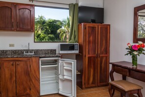 Une cuisine compacte dotée de meubles en bois, d’un four à micro-ondes, d’un réfrigérateur et d’une fenêtre donnant sur un paysage verdoyant.