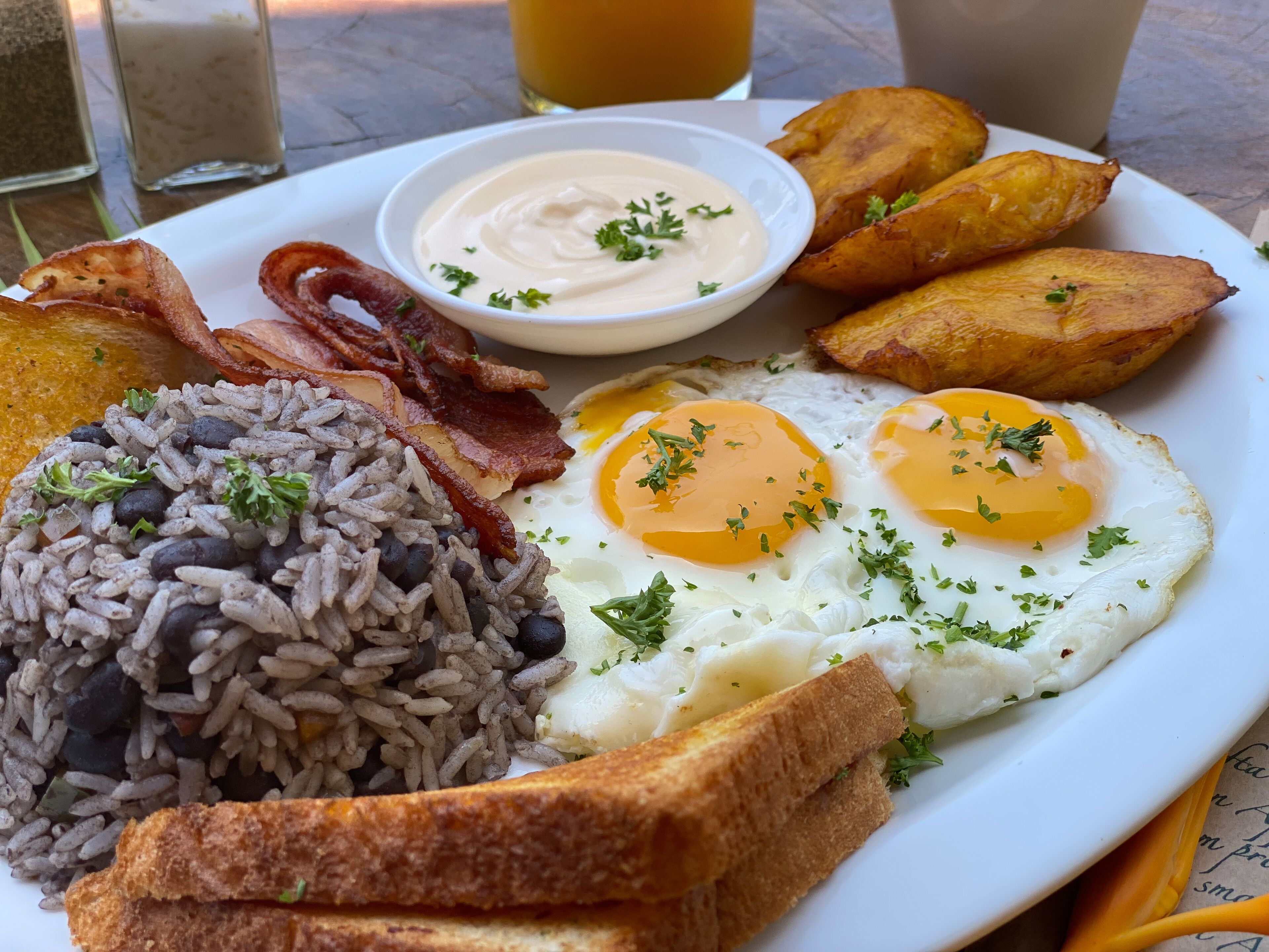 Um prato de comida de café da manhã com ovos fritos, feijão preto, torradas, batatas fritas e bacon.