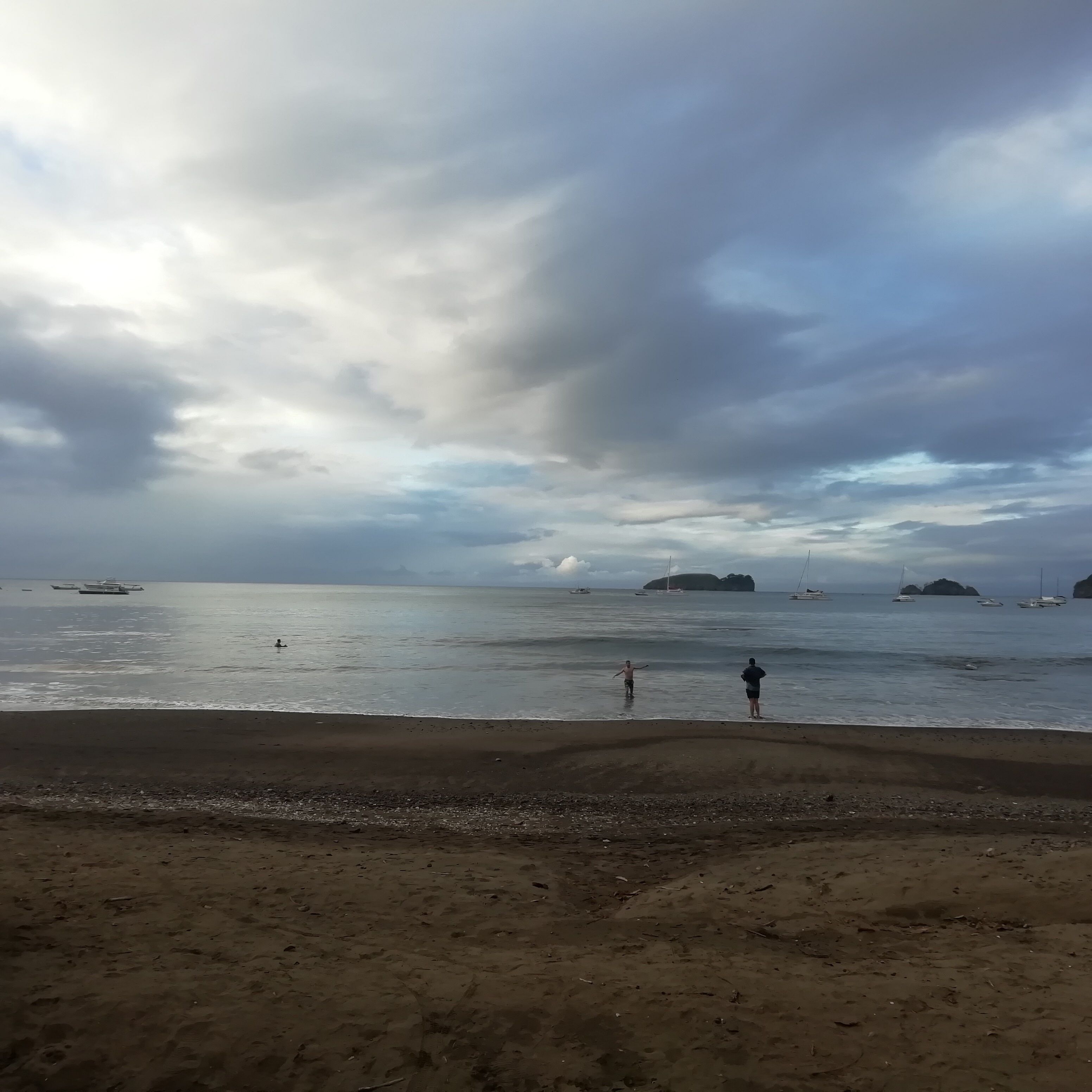 A beach with boats in the water and a cloudy sky.