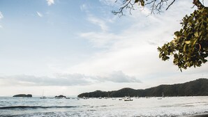 A beach with boats and a forested hill in the background.