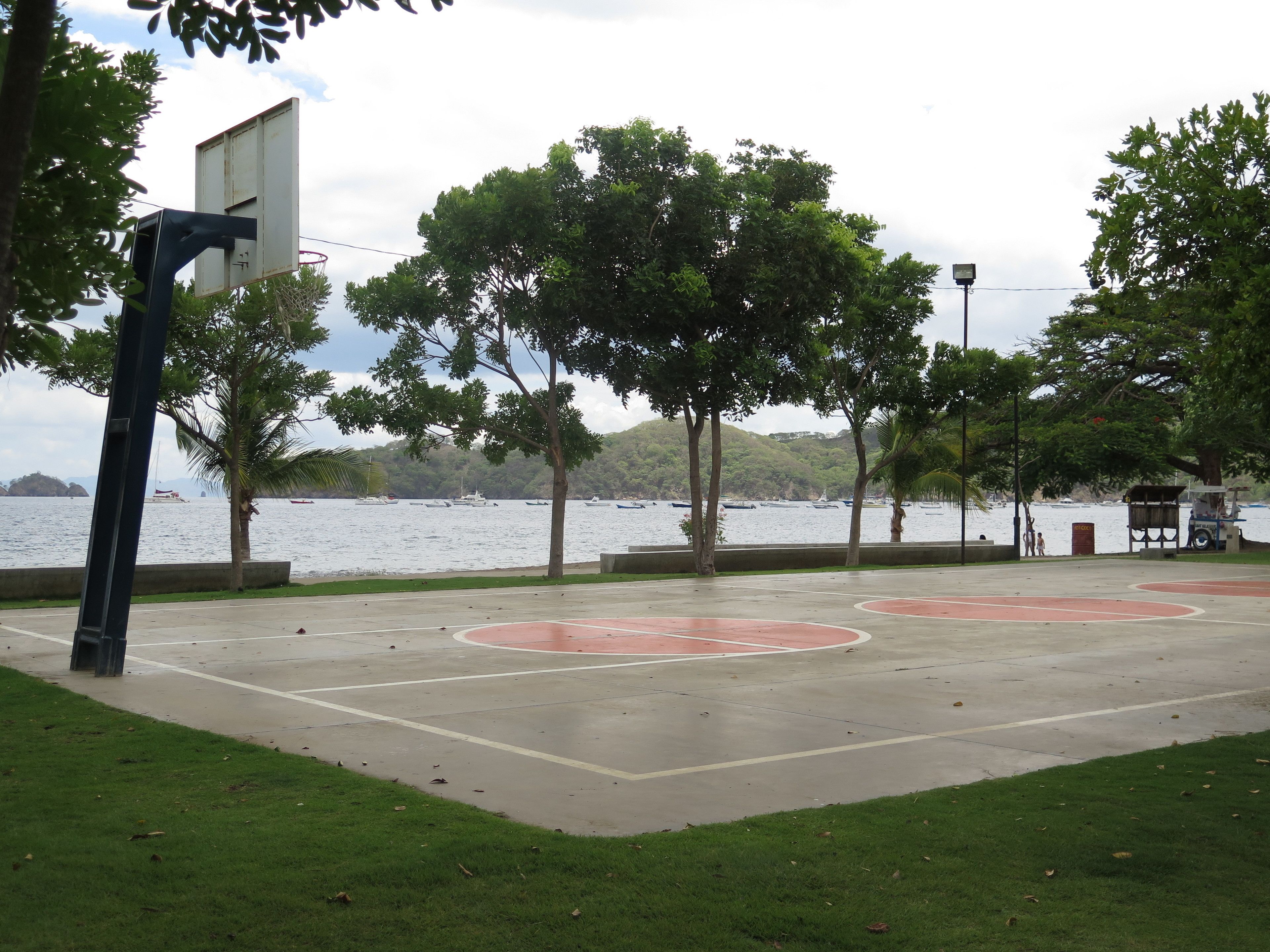 An outdoor basketball court with a view of the water and trees.