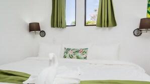 A neatly made bed with a green blanket, a floral pillow, and a towel draped over the side.