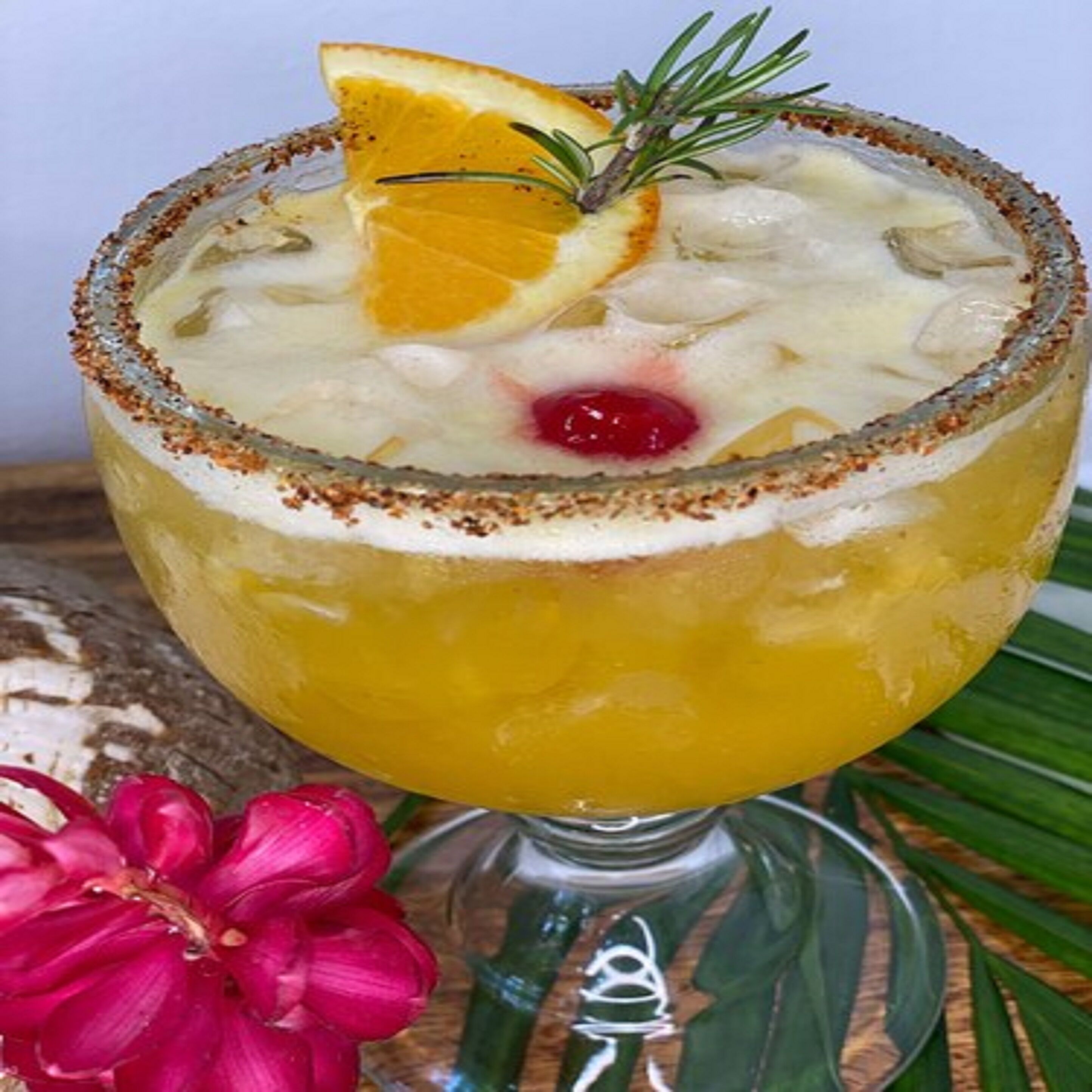 Un cóctel en un vaso con borde de sal, adornado con una rodaja de naranja y una ramita de romero.