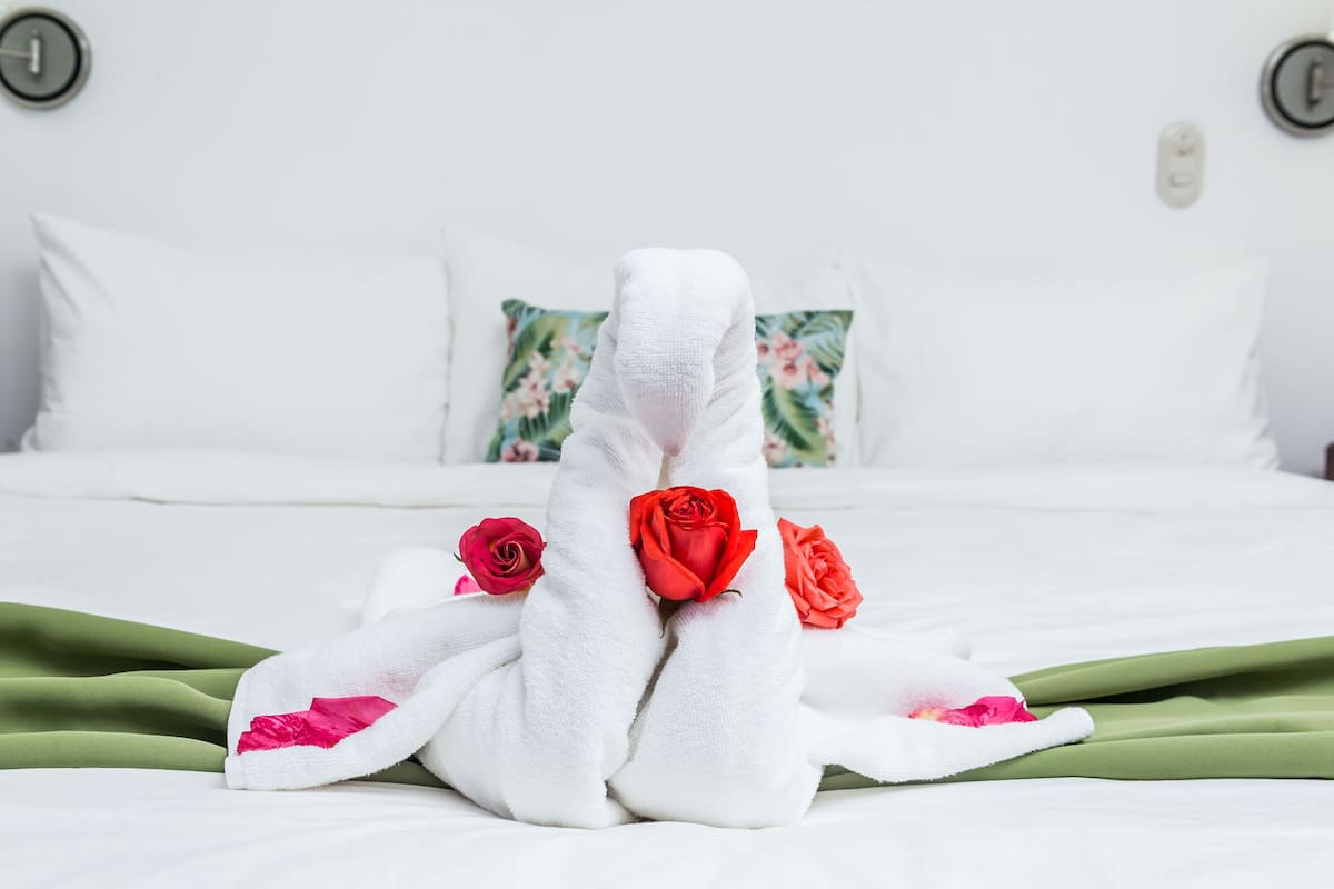 A neatly made bed with white linens and red roses.
