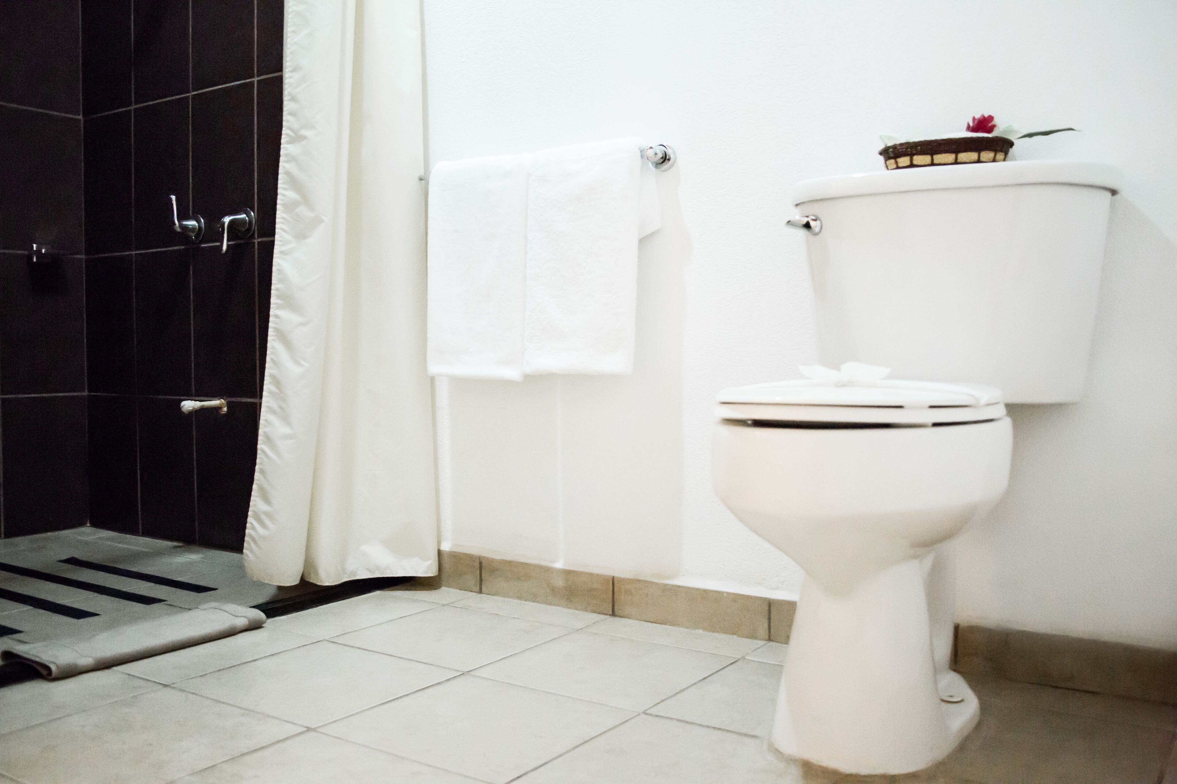 Um banheiro com vaso sanitário branco, cortina de chuveiro e piso ladrilhado.