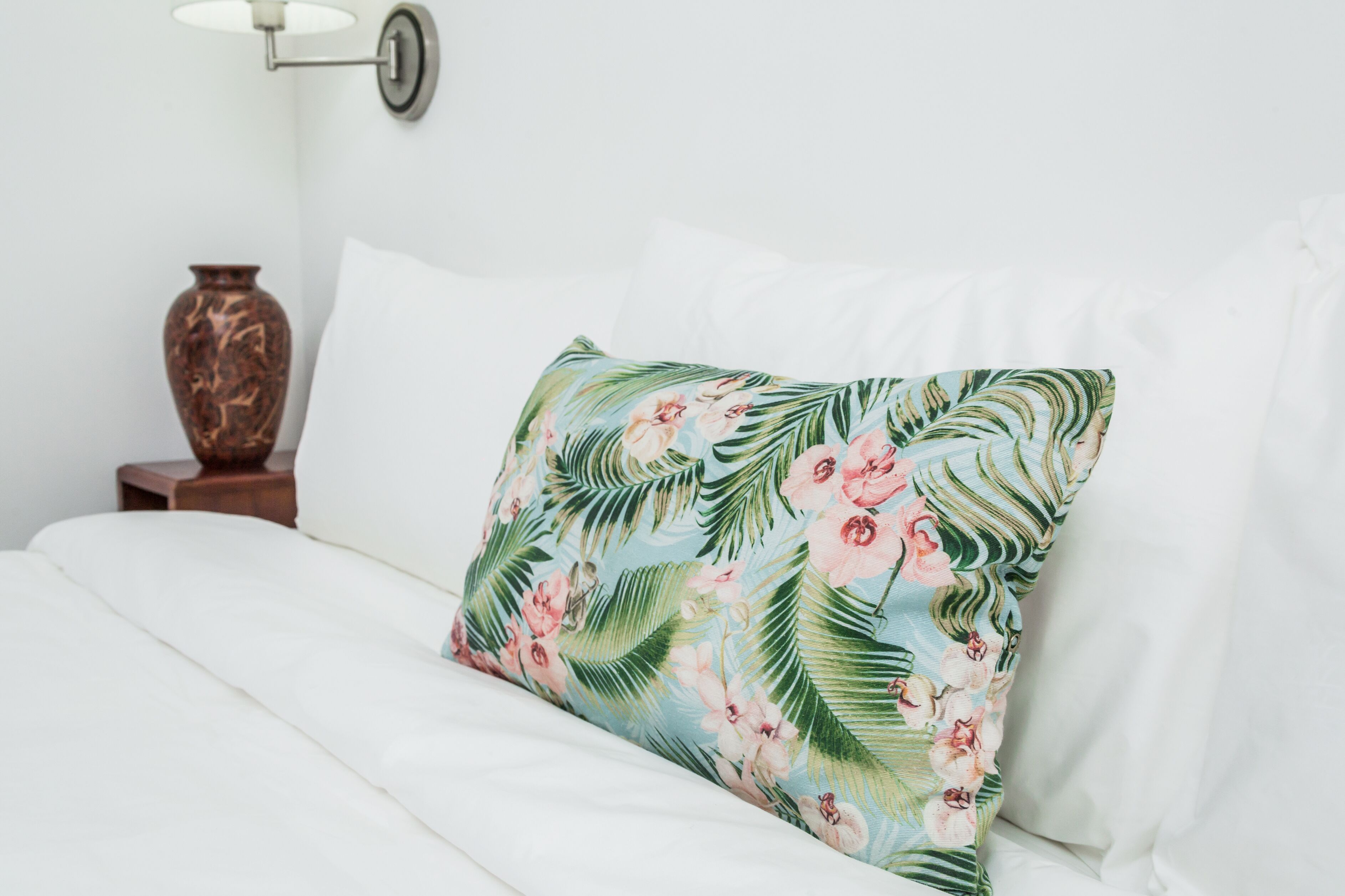 A bed with white bedding and a floral pillow.