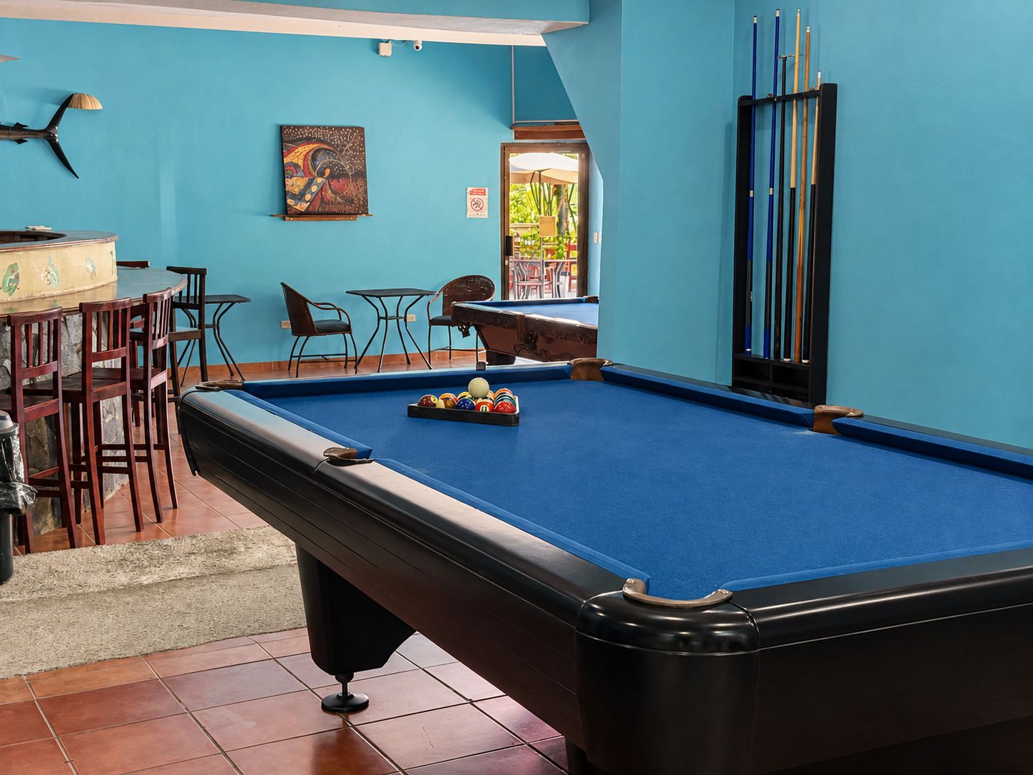 A pool table with balls, chairs, and a table with a painting on the wall.