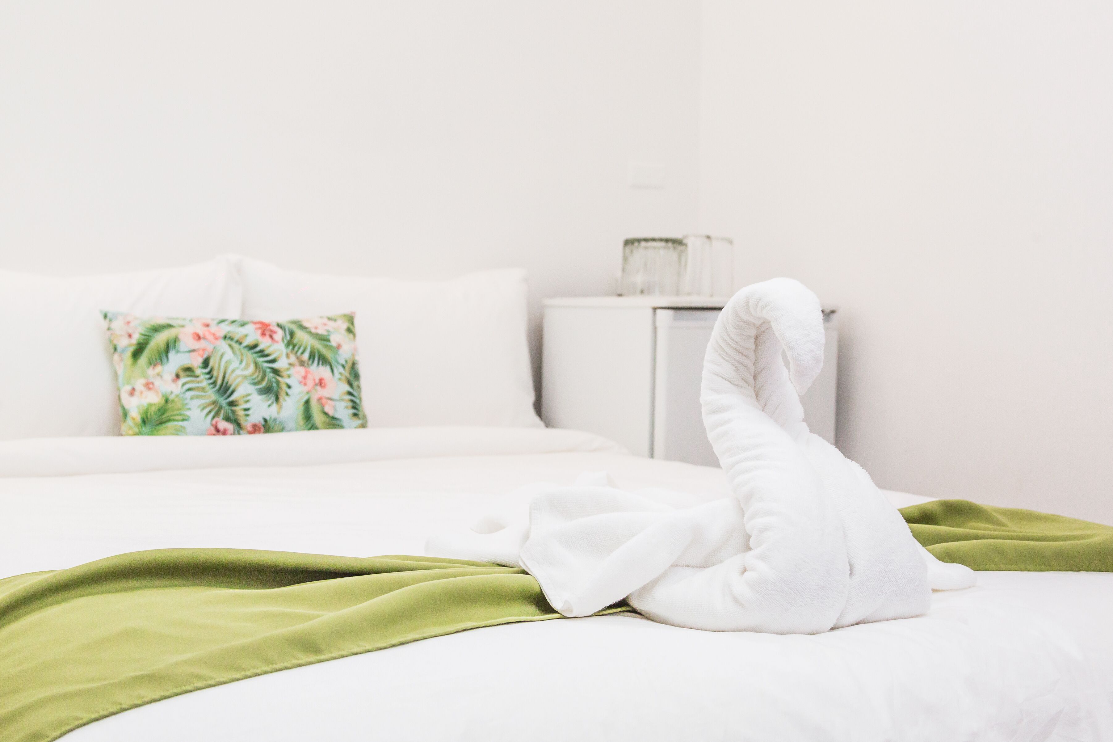Un lit bien fait, avec des draps blancs, un plaid vert et un coussin à motifs floraux.
