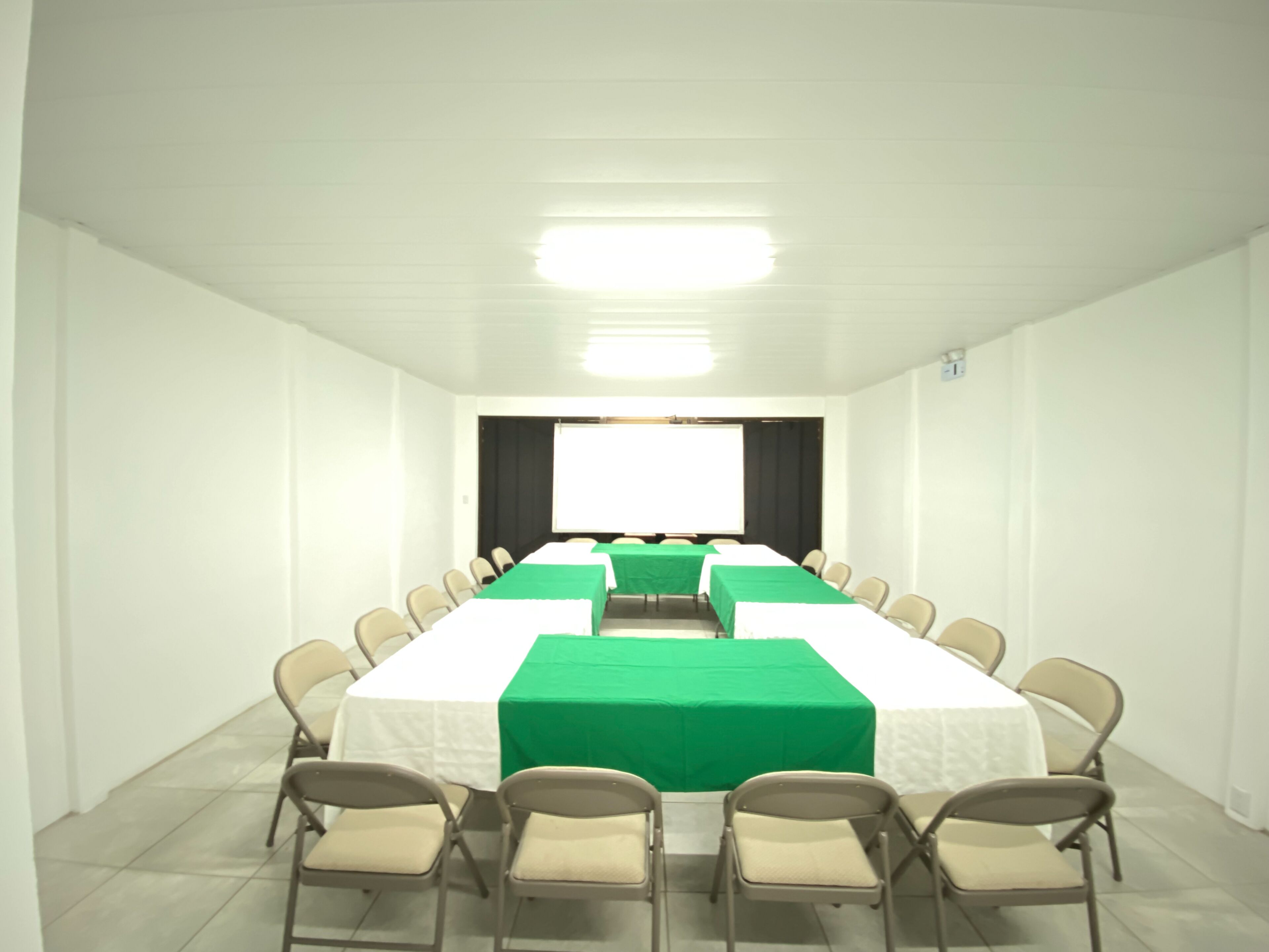 Un salón de conferencias con una larga mesa, sillas y una pantalla de proyector.
