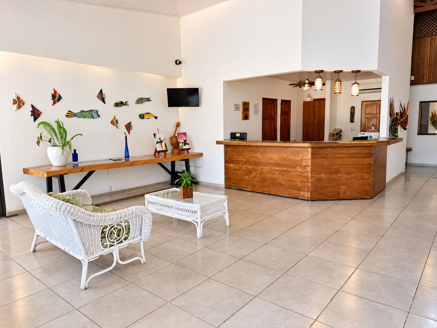 Uma área de recepção com uma mesa de madeira, duas cadeiras de vime brancas, uma TV de tela plana e obras de arte nas paredes.