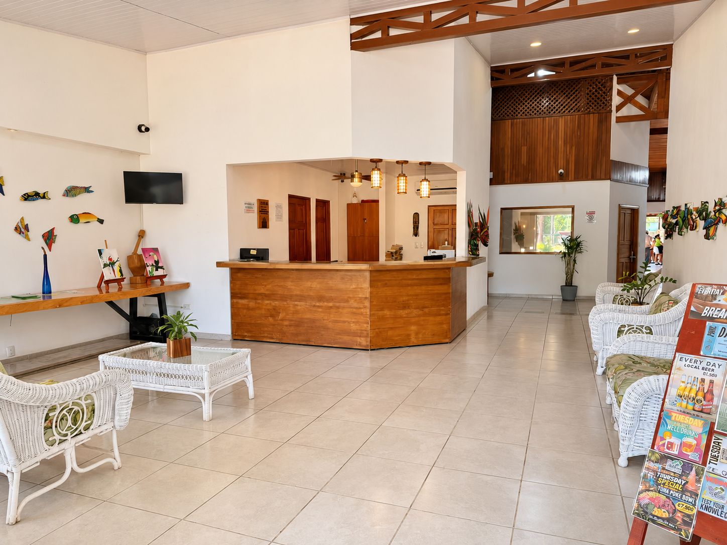 A hotel lobby with a reception desk, white wicker furniture, and artwork on the walls.