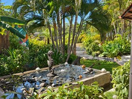 Un jardín tropical con un estanque, estatuas de piedra y abundante vegetación.