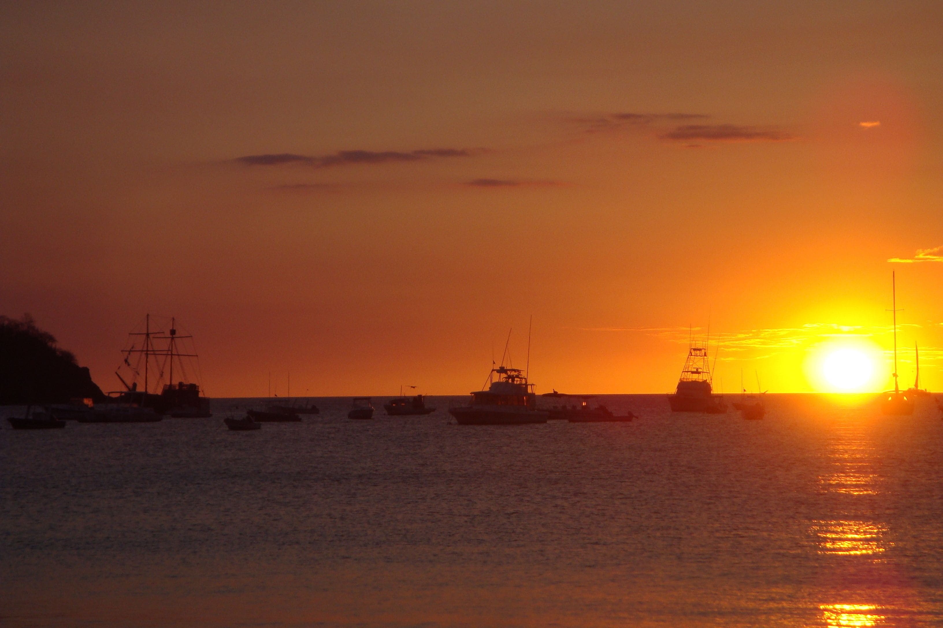 A sunset over a calm sea with several boats.