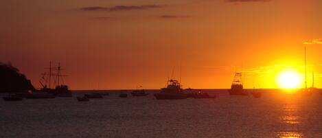 A sunset over a calm sea with several boats.