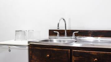 A kitchen with a stainless steel sink, two wooden drawers, and three clear glasses on a white countertop.