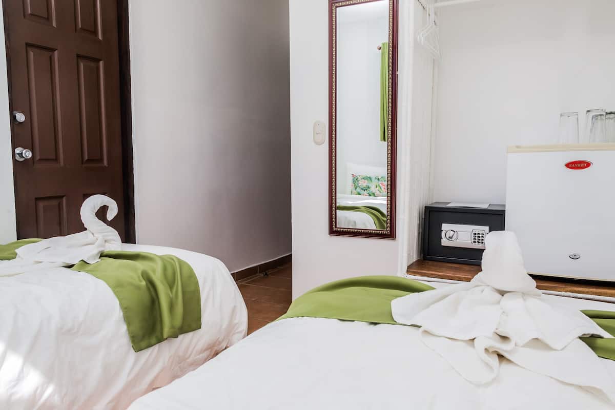 A hotel room with two beds, a mirror, a minibar, and a door.