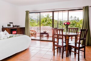 Una habitación de hotel con cama, una mesa de comedor con sillas, vistas al exterior y un microondas en la cómoda.