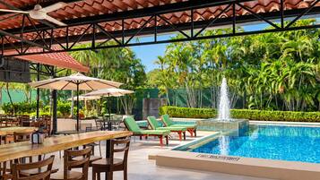 Un espace extérieur avec une piscine, des chaises longues, une table à manger avec des chaises et des parasols.