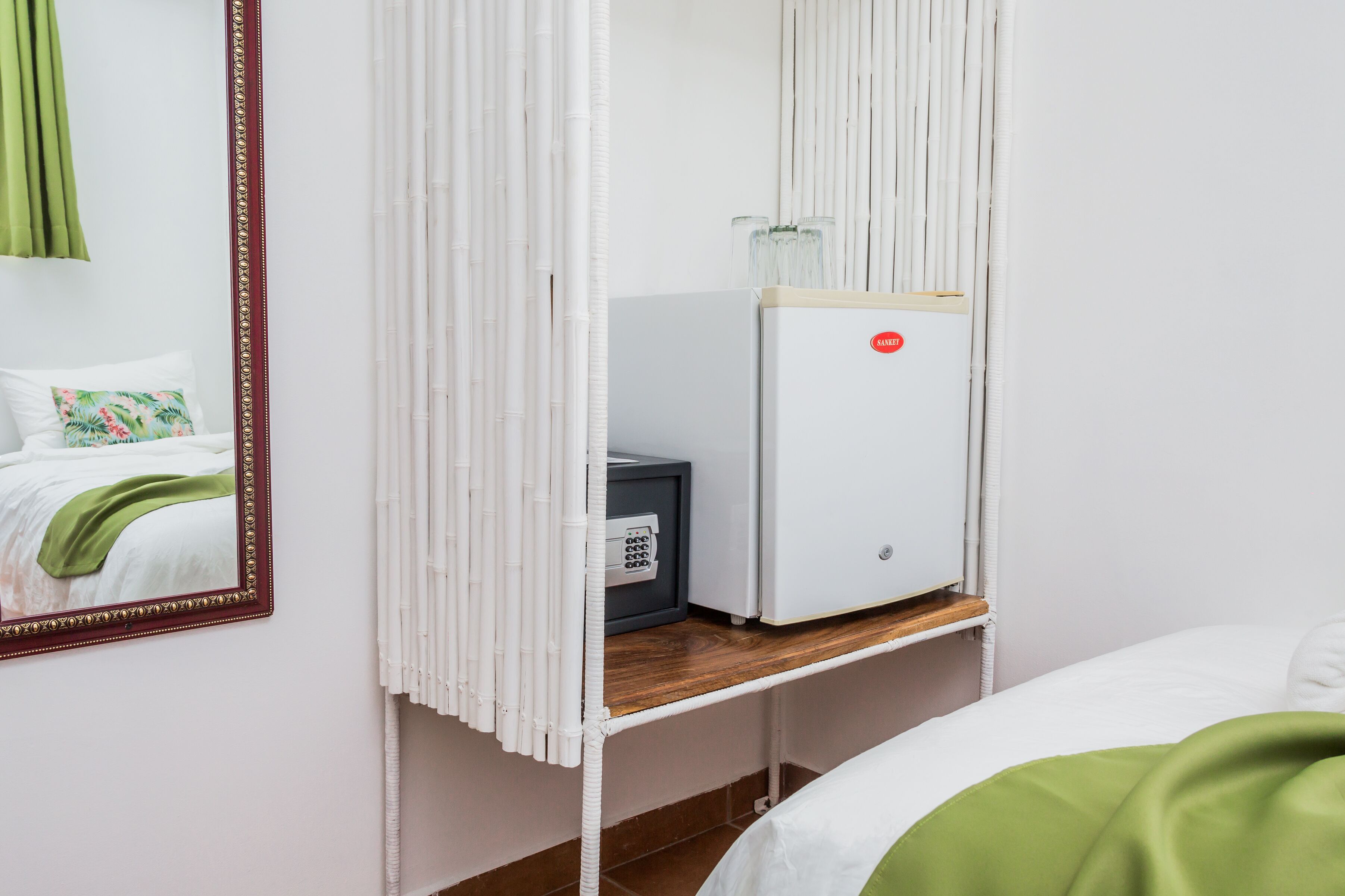 Habitación de hotel con cama, espejo, minibar y ventana con persianas.