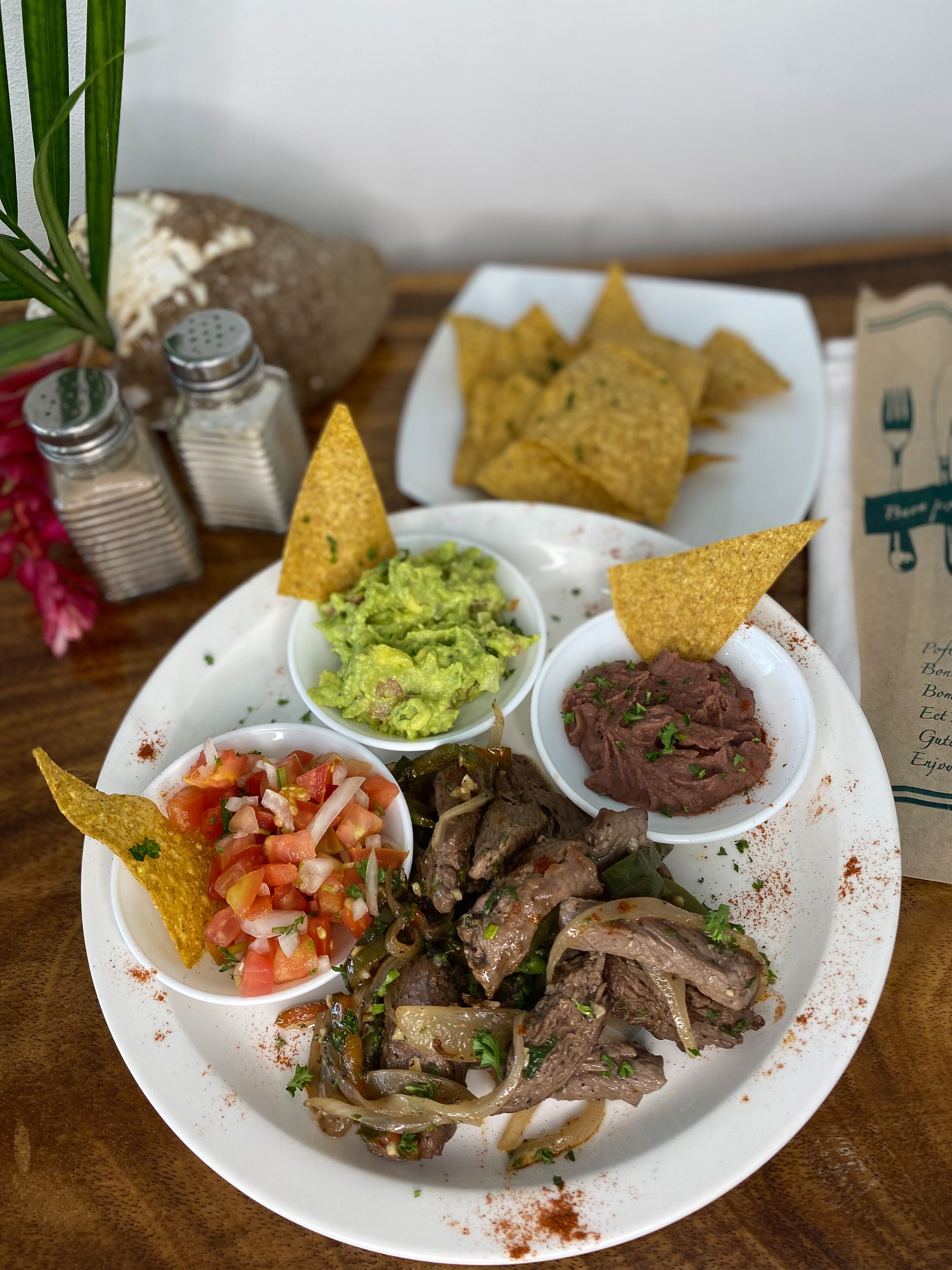 En tallerken med mad, bestående af nachos, guacamole, salsa, refried bønner og grillet kød.