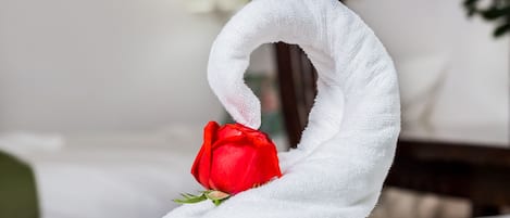 A neatly made bed with a white towel shaped like a swan, holding a red rose.