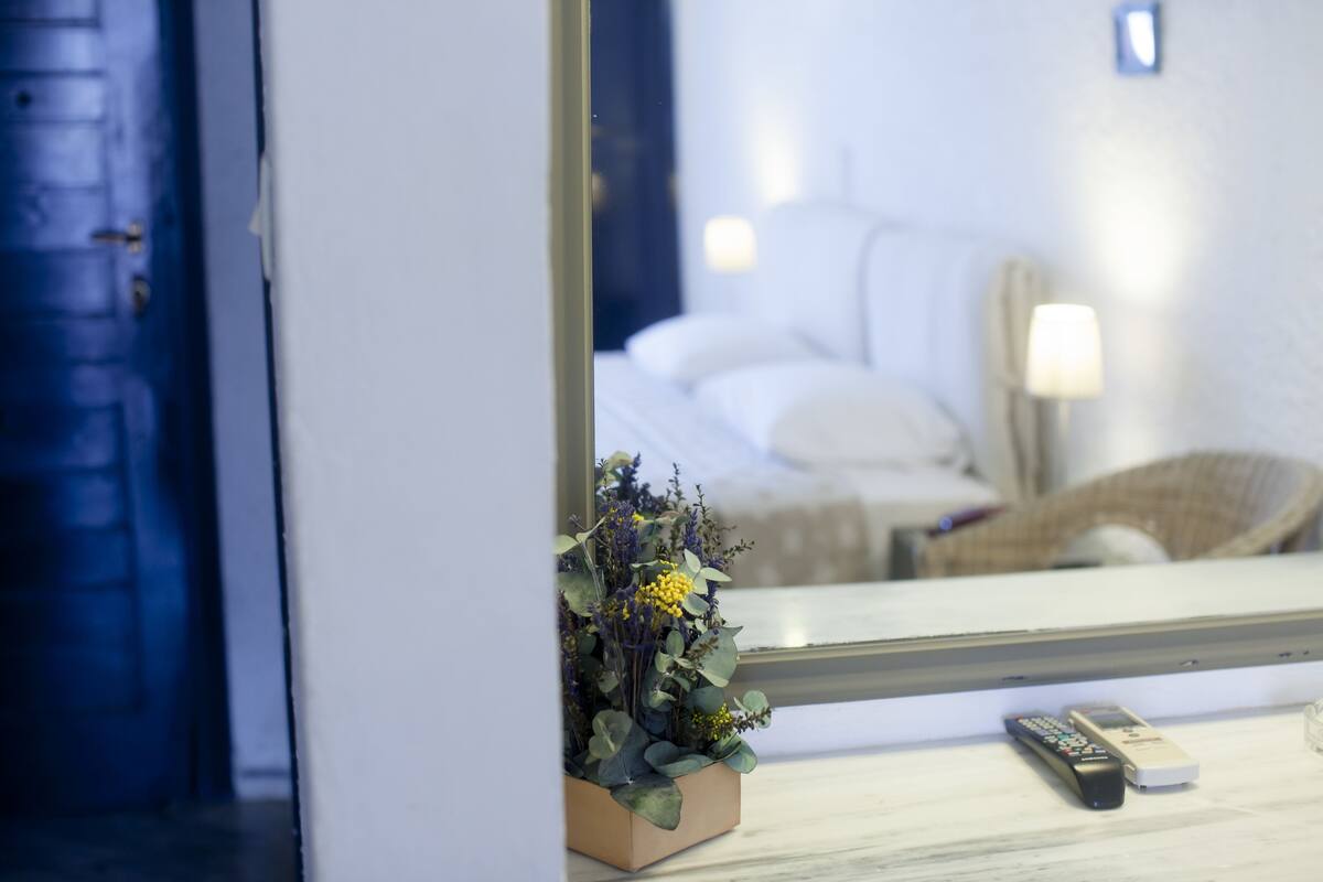 Een slaapkamer met een bed, nachtkastje, lamp en een potplant.